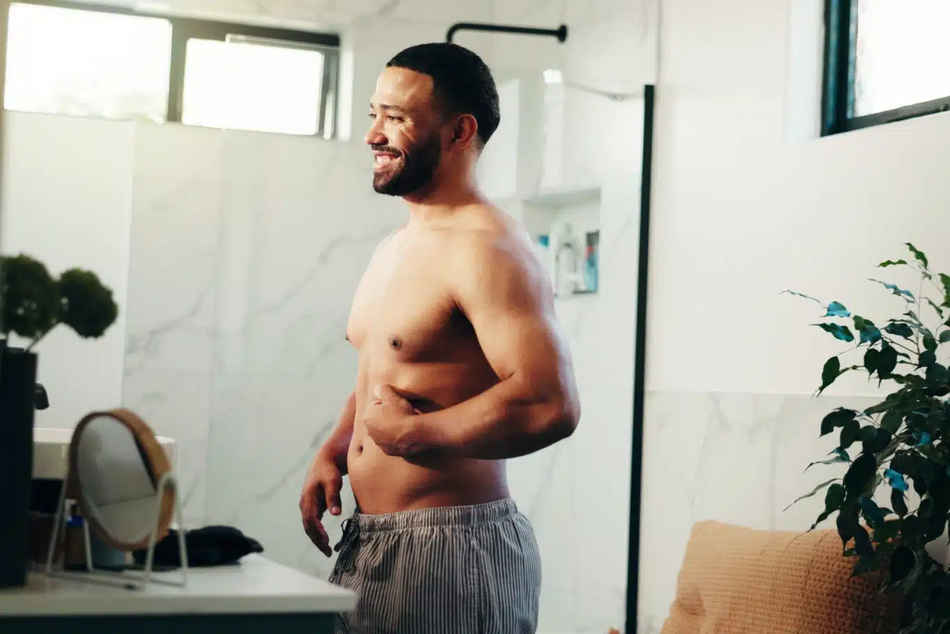 male body confidence Man smiling at mirror in bathroom checking breast reduction surgery results.